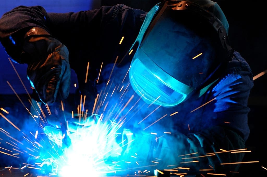 A person welding, wearing a welding mask and gloves for safety.